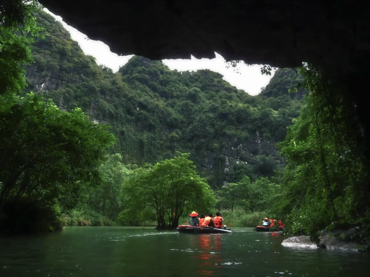 Boats leaving a limestone cave onto a green river